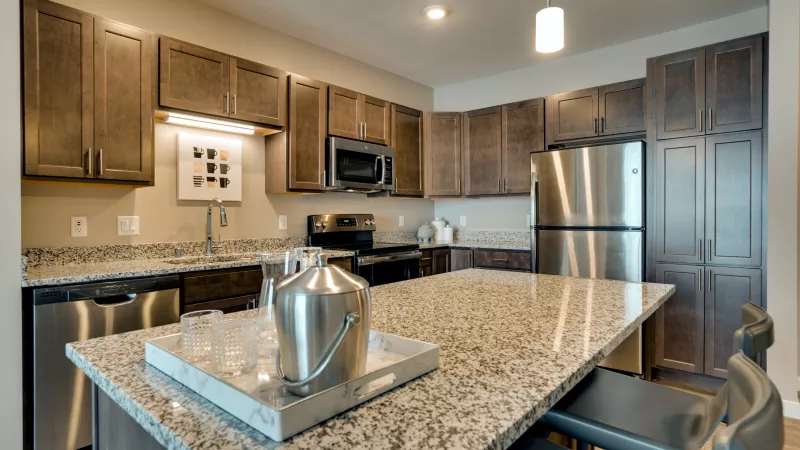 Modern kitchen featuring dark wood cabinets, granite countertops, stainless steel appliances, and an island with bar stools.